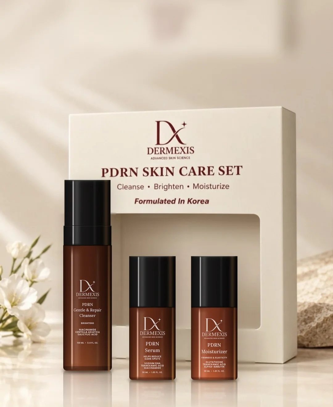 The Dermexis PDRN Skin Care Set box with the cleanser, serum and moisturizer in front, beside white flowers and stone
